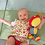 Inaya participe au concours pour gagner de l'argent avec cette photo : baby, child, smiling, toy, stuffed_animal, colorful, patterned_clothing, heart_pattern, tulip_pattern, red_shorts, padded_surface, playful, happy, cute, infant, lying_down, indoors, bright, cheerful, person