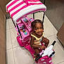 child, girl, toy_scooter, pink, indoor, smiling, braided_hair, beads, floor_tile, playful, canopy, toy, vehicle, happy, person, cute, colorful, young, small, seated