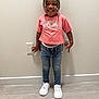 child, smiling, standing, jeans, white_sneakers, pink_shirt, beads, hair, indoor, wall, floor, person, cute, happy, fashion, accessory, necklace, bracelet, casual, portrait