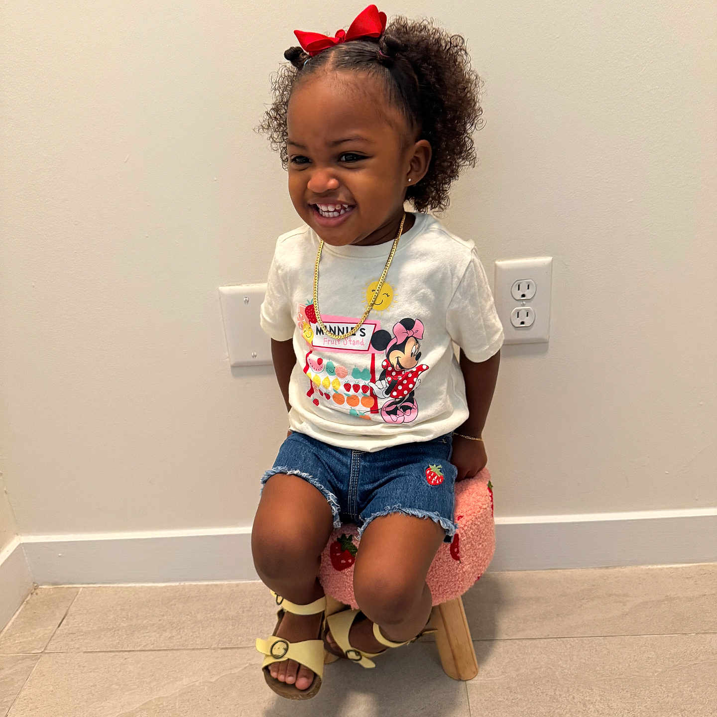 Yomi is registered to the contest to win money with this photo: child, curly_hair, cute, denim_shorts, floor_tiles, girl, gold_chain, happy, indoor, jewelry, minnie_mouse, playful, red_bow, sandals, sitting, smiling, stool, strawberry_patch, tshirt, wall_outlet
