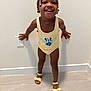 Yomi is registered to the contest to win money with this photo: toddler, child, smiling, braids, beads, yellow_outfit, minnie_mouse, sandals, standing, happy, indoor, floor, wall, playful, cute, person, portrait, young_child, fashion, feet