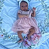 baby, infant, child, pink_dress, headband, blanket, floral_pattern, soft_texture, lying_down, curious_expression, indoors, small_hands, small_feet, cute, adorable, portrait, one_person, young, toddler, fabric