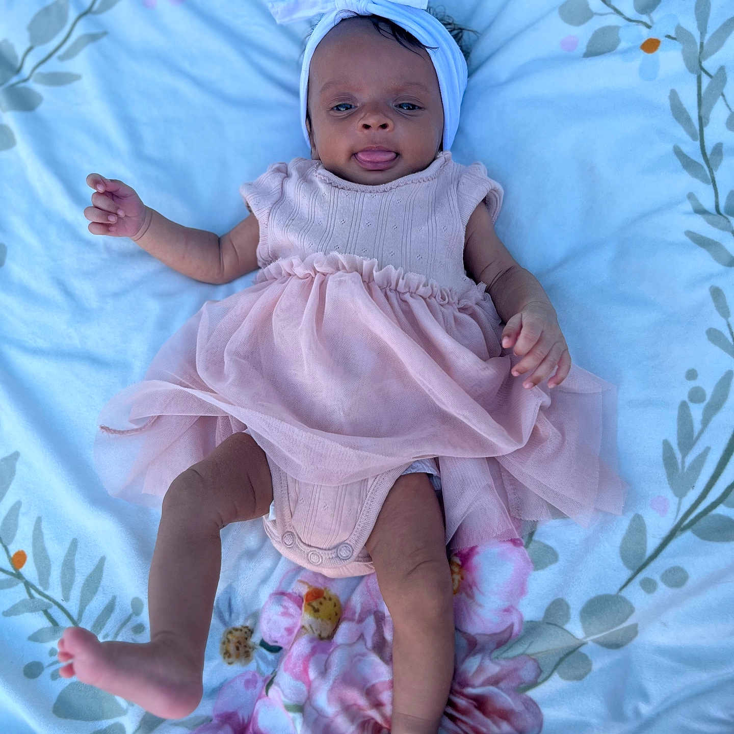 Kaylyn is registered to the contest to win money with this photo: baby, infant, child, girl, pink_dress, headband, blanket, floral_pattern, lying_down, tongue_out, cute, playful, skin, limbs, indoors, soft_lighting, portrait, adorable, young_child, smiling
