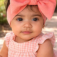 Kimberly is registered to the contest to win money with this photo: adorable, baby, blurred_background, bow, brown_eyes, cheeks, closeup, dress, earring, eyelashes, fashion, gingham, headband, outdoor, pink, portrait, sitting, skin, smile, toddler