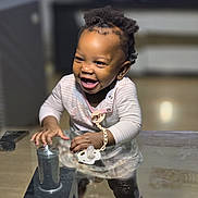 Geneviève a rejoint le concours — aidez-le/la à gagner de superbes lots ! baby, child, clothing, cute, earrings, furniture, glass_table, hair, happy, home, indoor, joyful, pacifier, person, playful, reflection, smiling, standing, twists, young