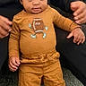 Jerome is registered to the contest to win money with this photo: toddler, child, curly_hair, standing, mustard_clothing, football_graphic, adult_hands, indoor, carpet, sofa, white_socks, cute, family, support, smiling, person, young_child, casual_wear, home, portrait