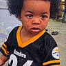 toddler, child, afro, jersey, steelers, sportswear, indoor, carpet, hand_holding, person, curious, black_hair, expression, living_room, casual, footwear, furniture, young_child, cute, portrait