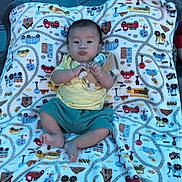 Logan joined the competition — help win amazing prizes! baby, infant, blanket, colorful, pattern, toy, pacifier, bed, clothing, yellow_shirt, blue_shorts, cute, lying_down, indoors, face, person, child, soft, warm, comfort