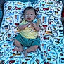 baby, infant, blanket, colorful, pattern, toy, pacifier, bed, clothing, yellow_shirt, blue_shorts, cute, lying_down, indoors, face, person, child, soft, warm, comfort