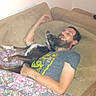 arm, beard, blanket, brown, casual, comfort, companion, couch, dog, floral_pattern, furniture, home, human, indoor, man, pet, relaxing, resting, sleeping, tshirt