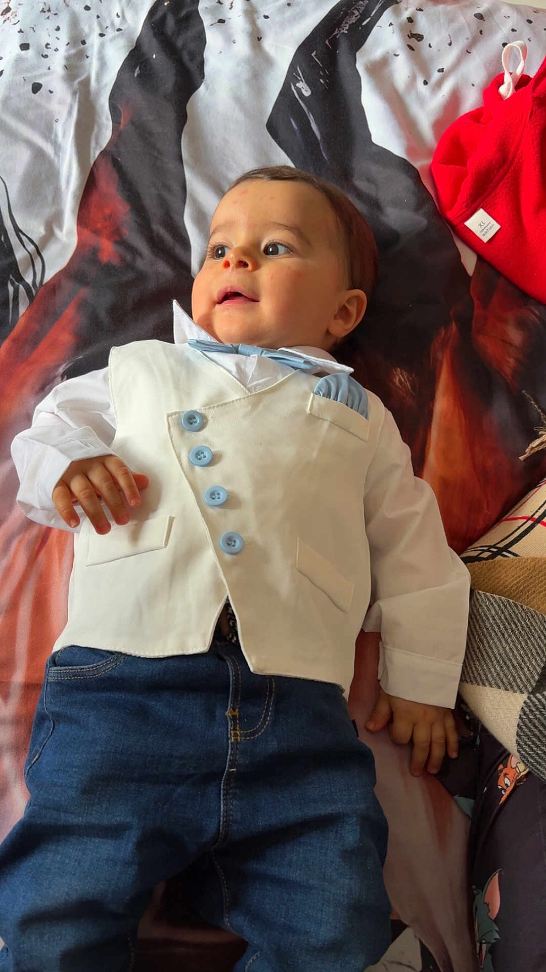 Timéo participe au concours pour gagner de l'argent avec cette photo : baby, child, infant, vest, bow_tie, blue_buttons, jeans, lying_down, bedspread, patterned, curious, face, hand, clothing, indoor, cute, small, casual, portrait, adorable