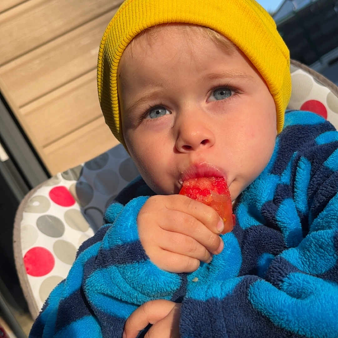 Laydon a rejoint le concours — aidez-le/la à gagner de superbes lots ! blue_eyes, blue_sky, child, closeup, cute, expression, face, fleece_jacket, food, hand, high_chair, outdoor, popsicle, portrait, snack, summer, sunlight, toddler, warm_clothing, yellow_beanie
