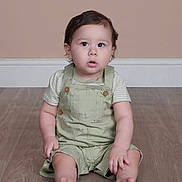 Jayden is registered to the contest to win money with this photo: child, toddler, baby, sitting, floor, overalls, striped_shirt, barefoot, curly_hair, indoors, wooden_floor, expression, portrait, casual_clothing, young_child, cute, innocent, curious, light_green, neutral_background