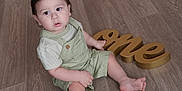 Jayden joined the competition — help win amazing prizes! toddler, child, baby, floor, wooden_floor, overalls, green_clothing, striped_shirt, barefoot, indoor, celebration, birthday, sign, golden_sign, one, sitting, curious, young_child, portrait, person