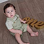 toddler, child, baby, floor, wooden_floor, overalls, green_clothing, striped_shirt, barefoot, indoor, celebration, birthday, sign, golden_sign, one, sitting, curious, young_child, portrait, person