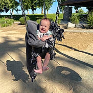 Logan is registered to the contest to win money with this photo: baby, blanket, chain, child, daylight, foot, grass, happy, nature, outdoor, park, pavilion, person, playground, sand, shadow, smiling, sunlight, swing, trees