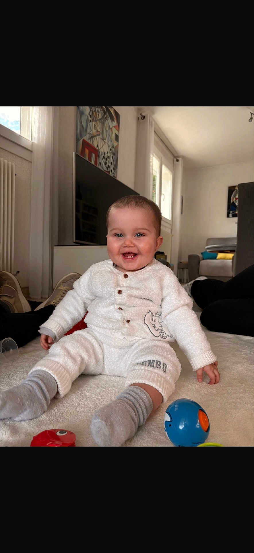 Kaylee a rejoint le concours — aidez-le/la à gagner de superbes lots ! baby, smiling, white_pajamas, elephant_design, gray_socks, toys, living_room, television, couch, blanket, floor, window, natural_light, happy, infant, child, person, indoor, seated, cute