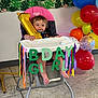 Addison is registered to the contest to win money with this photo: baby, high_chair, balloon, birthday, celebration, colorful, streamers, party, toddler, indoor, decorations, floor, smiling, person, foot, leaf_pattern, wall, chair, pink, number_one
