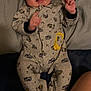baby, infant, smiling, onesie, clothing, bed, blanket, person, happy, cute, lying_down, child, sleepwear, footed_pajamas, indoors, newborn, face, expression, hand, comfort
