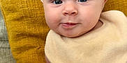 Eliza is registered to the contest to win money with this photo: baby, infant, child, face, eyes, smile, bib, clothing, floral, pillow, yellow, couch, skin, hand, portrait, indoors, cute, soft, young, person