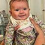 baby, infant, smile, face, hands, tattoo, floral_clothing, onesie, bib, indoor, person, cute, child, closeup, expression, happy, holding, skin, portrait, young