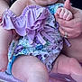 baby, child, infant, floral_clothing, lavender, hat, blue_eyes, hand_holding, adult_hand, rings, nail_polish, inflatable_seat, pink, skin, face, legs, toes, person, closeup, outdoor