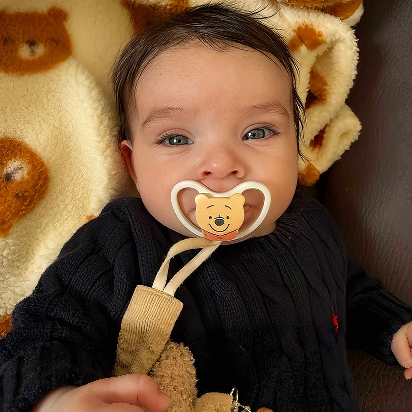 Gianna a rejoint le concours — aidez-le/la à gagner de superbes lots ! baby, pacifier, blanket, bear_pattern, black_sweater, hand, blue_eyes, face, cute, infant, cozy, soft_toy, indoor, child, portrait, smiling, closeup, skin, fingers, clothing