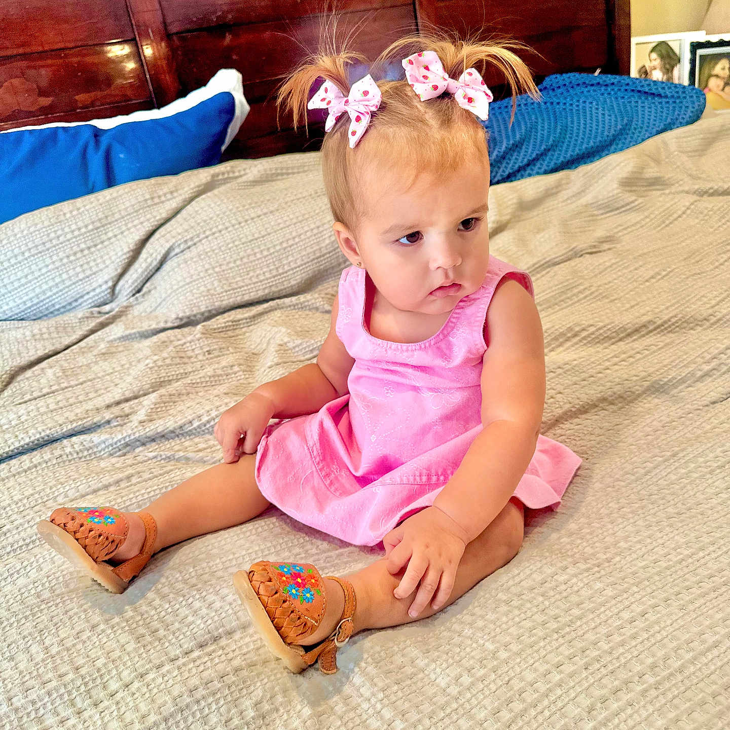 Clarissa joined the competition — help win amazing prizes! bed, blanket, child, curious_expression, cute, footwear, framed_photos, girl, hair_bows, home, indoor, nightstand, pillow, pink_dress, portrait, sandals, sitting, toddler, wooden_headboard, young_child