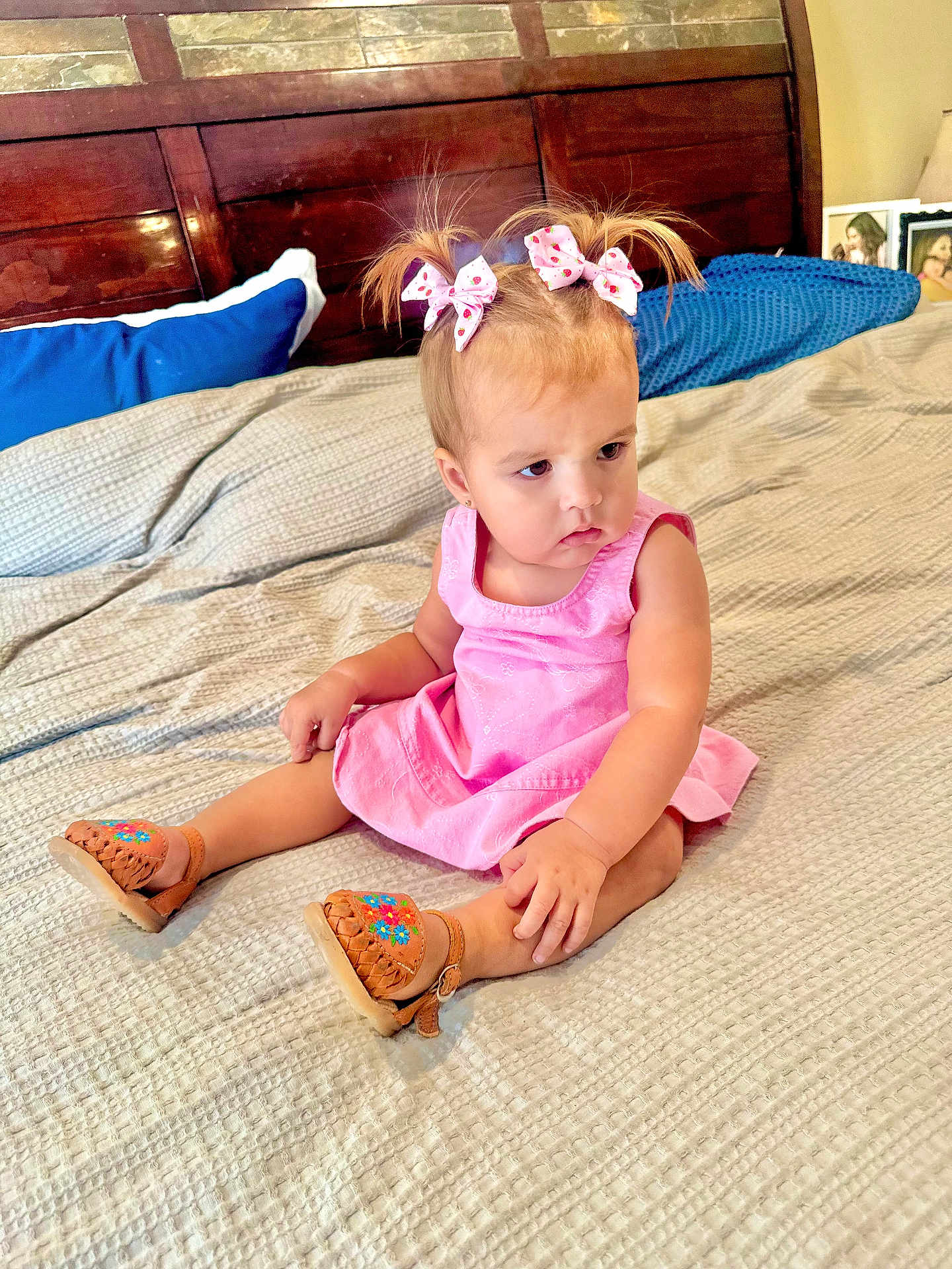 Clarissa joined the competition — help win amazing prizes! toddler, child, girl, pink_dress, hair_bows, bed, blanket, sandals, wooden_headboard, pillow, indoor, curious_expression, framed_photos, nightstand, home, sitting, footwear, cute, young_child, portrait