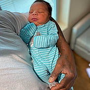 David is registered to the contest to win money with this photo: newborn, baby, infant, sleeping, portrait, indoors, onesie, turquoise, striped_clothing, adult, hand, arm, tattoo, cradled, couch, blanket, window, blinds, peaceful, family