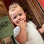 toddler, child, indoor, curly_hair, white_shirt, hand_on_mouth, wooden_wall, crib, green_wall, red_wall, flooring, baby, portrait, smiling, person, furniture, home, cute, playful, young_child