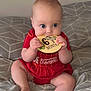 baby, infant, red_clothing, bed, blanket, plaque, wooden, sitting, chewing, cute, child, hands, feet, blue_eyes, patterned_bedspread, indoors, portrait, crawling_age, teething, smiling