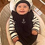 anchor_emblem, baby, baby_chair, black_dress, child, cozy, cushion, cute, happy, hat, headwear, indoor, infant, long_sleeves, person, portrait, sitting, smiling, striped_clothing, toddler