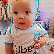 Sayan a rejoint le concours — aidez-le/la à gagner de superbes lots ! baby, child, infant, person, clothing, indoor, sports_jersey, uber_eats, curious, seated, skin, face, hand, furniture, laundry, background, home, blue, white, cute