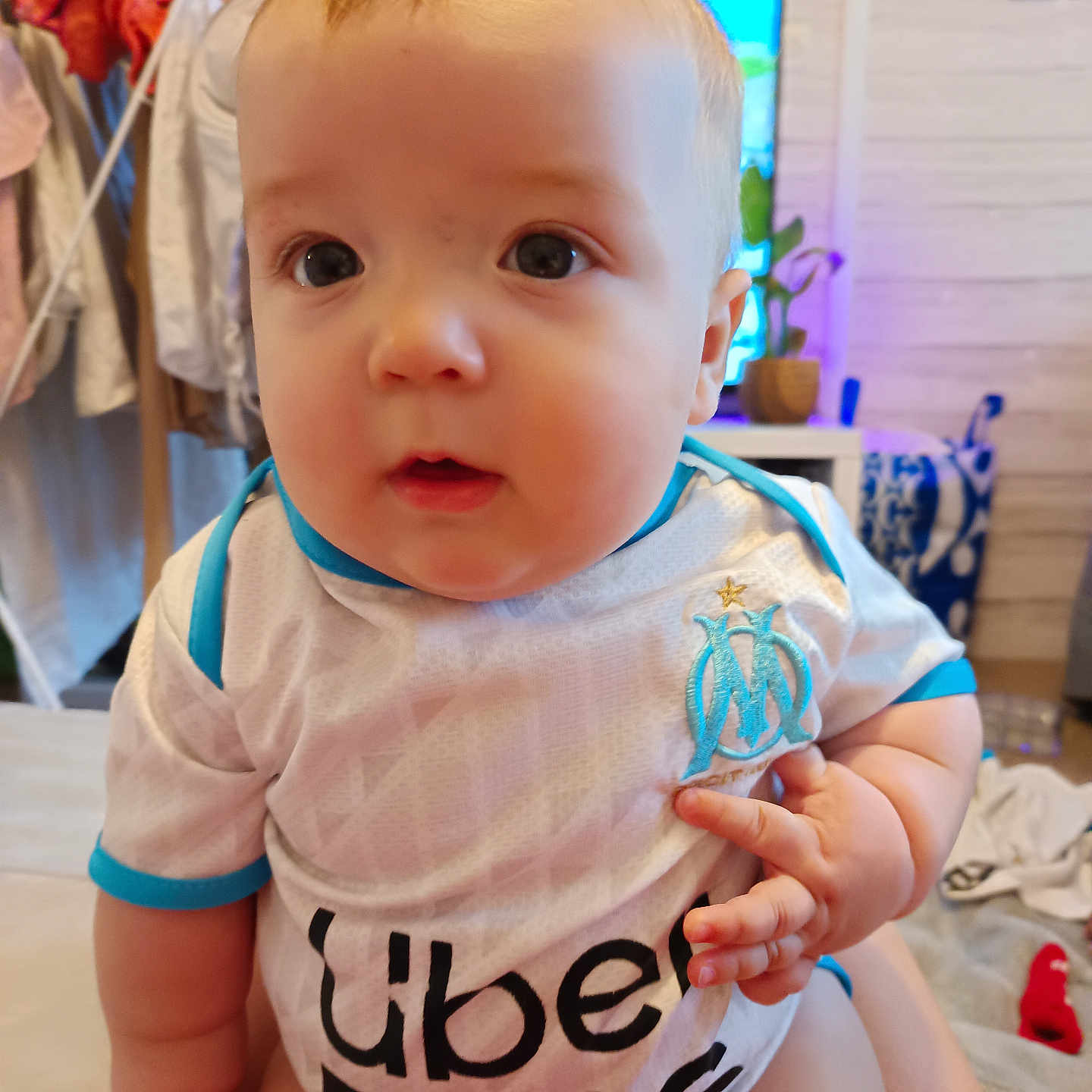 Sayan a rejoint le concours — aidez-le/la à gagner de superbes lots ! baby, background, blue, child, clothing, curious, cute, face, furniture, hand, home, indoor, infant, laundry, person, seated, skin, sports_jersey, uber_eats, white