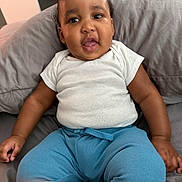 Micah is registered to the contest to win money with this photo: baby, child, infant, white_shirt, blue_pants, cushion, gray_cushion, sitting, indoors, curious_expression, cute, portrait, person, young_child, plump_arms, short_hair, skin, face, mouth_open, casual_clothing