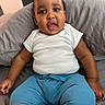 baby, child, infant, white_shirt, blue_pants, cushion, gray_cushion, sitting, indoors, curious_expression, cute, portrait, person, young_child, plump_arms, short_hair, skin, face, mouth_open, casual_clothing