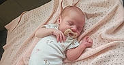 Star is registered to the contest to win money with this photo: baby, newborn, sleeping, blanket, pacifier, onesie, infant, soft, pink, cute, peaceful, resting, child, small, adorable, indoors, lying_down, cozy, portrait, human