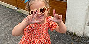 Naëlya participe au concours pour gagner de l'argent avec cette photo : child, curly_hair, cute, fashion, fence, floral_pattern, girl, hair_accessory, happy, heart_shaped, orange_dress, outdoor, pavement, playful, portrait, posing, sandals, smiling, summer, sunglasses