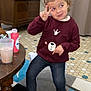 child, indoor, sitting, peace_sign, sweater, bear_face, curly_hair, shoes, polka_dot, bow, table, drink, carpet, floor_tiles, furniture, cage, playful, cute, person, smiling