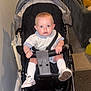 baby, stroller, indoor, child, socks, shoes, face, hands, clothing, seatbelt, carriage, person, floor, wall, radiator, couch, carpet, curious, expression, seated