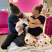 Teddy Keith is registered to the contest to win money with this photo: baby, beanie, bed, blanket, care, comfort, family, hospital, indoor, love, man, medical_equipment, newborn, pajamas, parent, phone, pink_wall, sitting, tattoo, woman