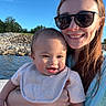 baby, child, woman, sunglasses, smile, outdoor, water, sky, cloud, rock, nature, holding, happy, casual_clothing, portrait, summer, people, baby_bib, shorts, daylight
