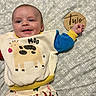 baby, infant, smiling, clothing, sweatshirt, animal_print, cow, blanket, pattern, wooden_sign, hand, face, cute, lying_down, child, happy, indoors, young, portrait, two_months