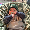 Weston is registered to the contest to win money with this photo: baby, pacifier, hat, green_beanie, blanket, patterned_blanket, sitting, infant, clothing, indoor, soft_furniture, child, cute, cozy, face, hands, comfortable, casual_wear, young_child, portrait