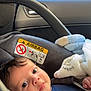 baby, car_seat, blanket, child, infant, seatbelt, car_interior, airbag_warning, soft_toy, portrait, face, young_child, safety, indoors, cute, comfort, looking_at_camera, clothing, head, close_up