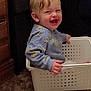 Austin is registered to the contest to win money with this photo: toddler, child, smiling, happy, indoor, plastic_basket, carpet, wooden_furniture, blue_sweater, person, cute, playful, blonde_hair, face, expression, sitting, hand, home, fun, joy