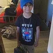 Antonio joined the competition — help win amazing prizes! child, boy, blue_beanie, black_tshirt, korea, indoor, lunchbox, sneakers, pants, smiling, standing, wooden_floor, chair, clothing, casual, living_room, door, young, person, accessory