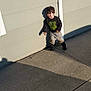 child, boy, shadow, wall, sidewalk, concrete, casual_clothing, sweatshirt, pants, boots, outdoor, sunlight, afternoon, playful, leaning, standing, young, hair, expression, background