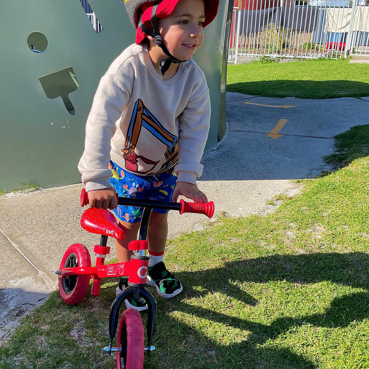 Jymarlee joined the competition — help win amazing prizes! activity, balance_bike, blue_sky, child, daylight, fence, grass, helmet, outdoor, person, playground, recreation, shadow, shoes, shorts, sidewalk, smile, sunlight, sweatshirt, toy